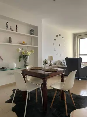 a living room with a wooden table and white chairs at Sunset Oasis: Beachfront Studio in Dubai