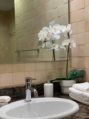 a bathroom sink with a mirror and white flowers at Sunset Oasis: Beachfront Studio in Dubai