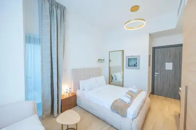 a white bedroom with a bed and a chair at Cozy Circle !Enjoyable Yet Affordable Studio Apartment! in Dubai
