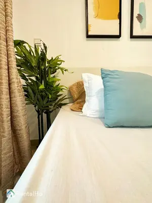 a white bed with a blue pillow and a plant at Quiet Studio with Balcony and Roof Top Pool in Dubai Marina in Dubai