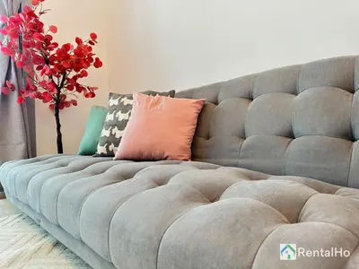 a gray couch with a pillow and a vase of flowers at Big Studio w/ Balcony and easy access to the Beach in Dubai