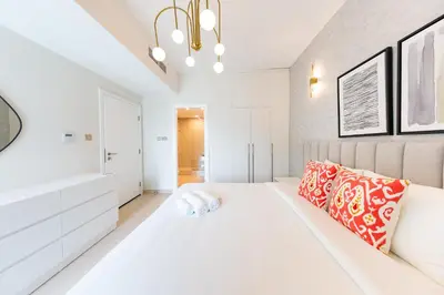a white bedroom with a large bed and a chandelier at Charming Brand New 2BR close to the Beach in Dubai