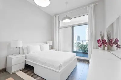 a white bedroom with a white bed and a window at ALiving Elegant & Cozy 1BR I Mazaya 11, Liwan in Dubai