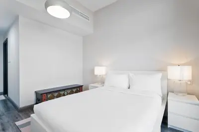 a white bedroom with a white bed and two lamps at ALiving Elegant & Cozy 1BR I Mazaya 11, Liwan in Dubai