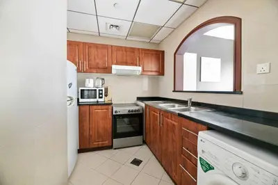 a kitchen with wooden cabinets and a white refrigerator at StoneTree - Cozy Fully-Furnished Studio in JLT in Dubai