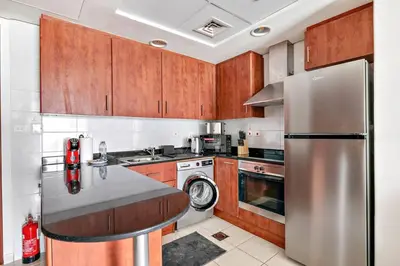 a kitchen with wooden cabinets and a stainless steel refrigerator at StoneTree - 1BR apartment with Lake View in Dubai