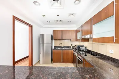 a kitchen with wooden cabinets and a stainless steel refrigerator at StoneTree - 1BR apartment with Beach Access Fairmont in Palm Jumeirah in Dubai