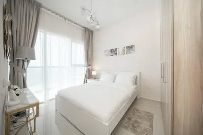 a white bedroom with a large bed and a window at StoneTree - Cozy 1BR with spacious balcony in Golf Vita A in Dubai