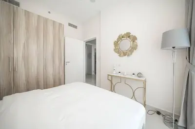 a white bedroom with a bed and a mirror at StoneTree - Cozy 1BR with spacious balcony in Golf Vita A in Dubai