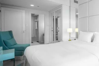 a white bedroom with a large bed and a blue chair at StoneTree - Furnished 1BR in Prime Location in Dubai