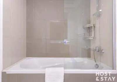 a white bath tub with a shower and a towel at Studio in Loreto 1A, DAMAC Hills - Host & Stay in Dubai