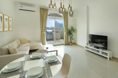 a white living room with a table and a tv at Plaza Residences - 2BR Apartment - Allsopp&Allsopp in Dubai