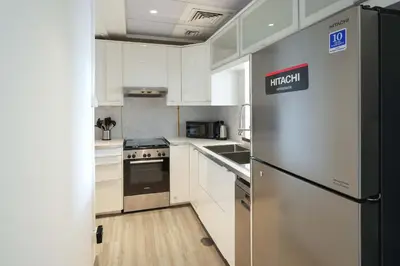 a kitchen with white cabinets and a stainless steel refrigerator at Plaza Residences - 2BR Apartment - Allsopp&Allsopp in Dubai