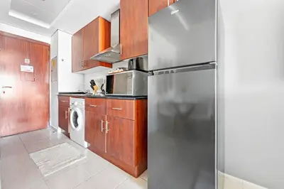 a kitchen with a stainless steel refrigerator and wooden cabinets at StoneTree - Furnished Studio Near Metro in Dubai