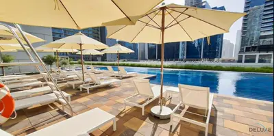 a pool with white chairs and umbrellas next to a building at Contemporary 1BR at Vera Tower Business Bay by Deluxe Holiday Homes in Dubai