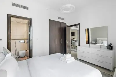 a white bedroom with a large bed and a bathroom at StoneTree - Furnished 1 BR in Bay Central in Dubai