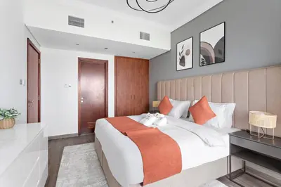 a bedroom with a large bed with an orange blanket at StoneTree - Amazing 1BR with Lake View in Dubai