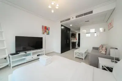 a white living room with a television and a couch at StoneTree - Fully Furnished Studio with Spacious Balcony in Dubai