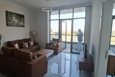 a person standing in a living room looking out the window at Dar Alsalam - Spacious and Bright 1BR Apartment in Majan in Dubai