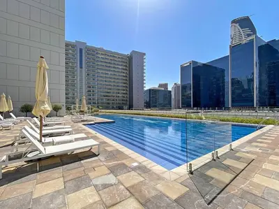 a swimming pool with chairs and umbrellas on a building at StoneTree - Modern 1BR Apartment in Vera Residence in Dubai