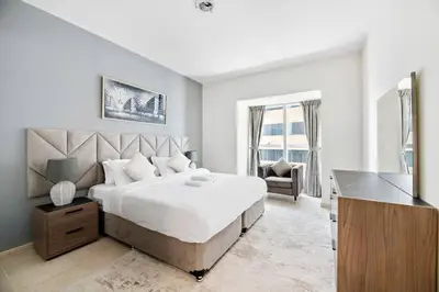 a white bedroom with a large bed and a desk at StoneTree - High Floor Furnished 1 BR in Dubai