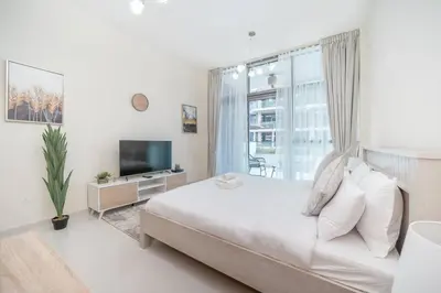 a white bedroom with a large bed and a television at StoneTree - Furnished Studio in Golf Promenade 3A in Dubai