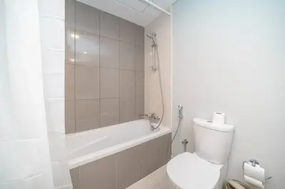 a white bathroom with a toilet and a bath tub at StoneTree - Furnished Studio in Golf Promenade 3A in Dubai