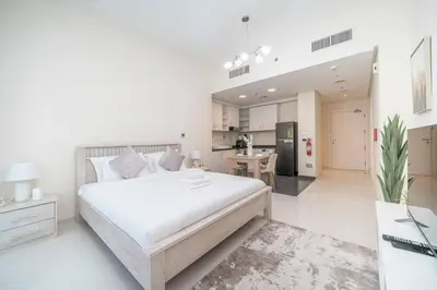 a white bedroom with a large bed and a kitchen at StoneTree - Furnished Studio in Golf Promenade 3A in Dubai
