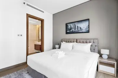 a bedroom with a large white bed and a mirror at StoneTree - Cozy 1 BR in Sobha Hartland Greens 1 in Dubai