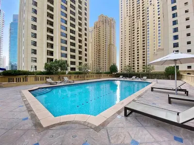 a large swimming pool with chairs and an umbrella at StoneTree - Near Beach - Furnished 1BR with Partial Sea View in Dubai