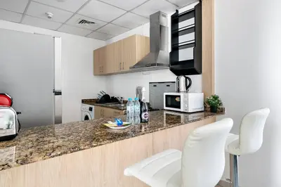 a kitchen with white chairs and a counter with a microwave at StoneTree - Furnished 1 BR Apartment Near to Tram in Dubai