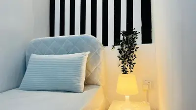 a bed with a pillow and a plant next to a lamp at Strips Partition Room Al barsha 1 Near MOE Metro in Dubai