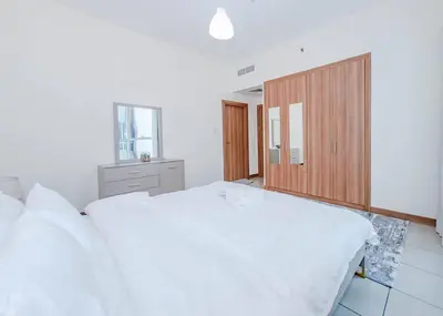 a bedroom with a white bed and a wooden cabinet at StoneTree - Spacious 1BR - Best Location for Tourist in Dubai