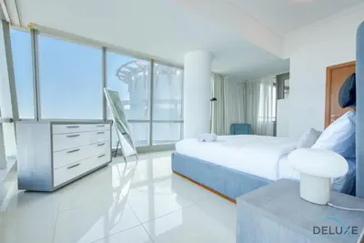 a white bedroom with a bed and a dresser and windows at Exquisite 3BR at Ocean Heights Dubai Marina by Deluxe Holiday Homes in Dubai