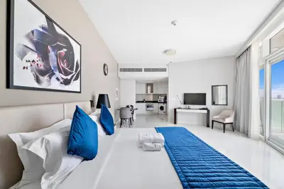 a bedroom with a large white bed with blue pillows at StoneTree - Stylish Studio Apartment in Damac Hills in Dubai