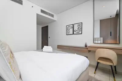 a white bedroom with a bed and a chair at Nasma Luxury Stays - Elegant 1BR With Stunning View of Park Avenue in Dubai
