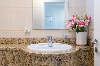 a bathroom sink with a mirror and a vase of pink flowers at Vibrant - Prime Location Dubai Marina - Near Metro in Dubai