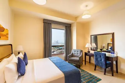 a hotel room with a bed and a desk and a window at Roda Amwaj Suites Jumeirah Beach Residence in Dubai