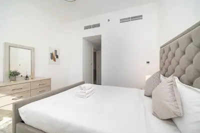 a white bedroom with a large bed and a mirror at StoneTree - Furnished 2BR with floor-to-ceiling window in Dubai
