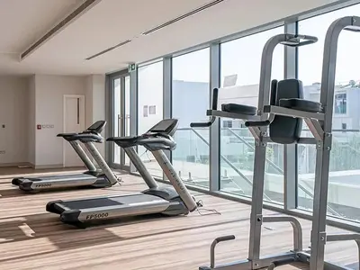 a gym with three tread machines in a room with windows at StoneTree - Furnished 2BR with floor-to-ceiling window in Dubai