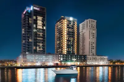 a boat in the water in front of two tall buildings at The First Collection Waterfront, Dubai, a Tribute Portfolio Hotel in Dubai