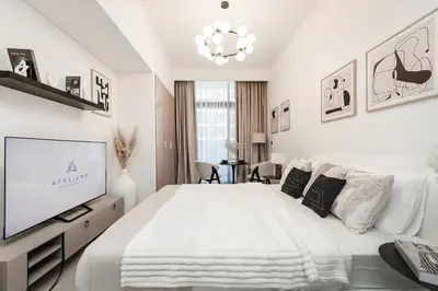 a white bedroom with a large bed and a tv at Modern studio in Azizi Riviera in Dubai