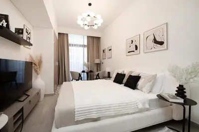 a white bedroom with a large bed and a chandelier at Modern studio in Azizi Riviera in Dubai