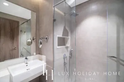 a bathroom with a shower with a sink and a mirror at LUX The District One Lagoon View Suite in Dubai