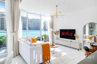 a living room with white furniture and a large window at LUX The District One Lagoon View Suite in Dubai
