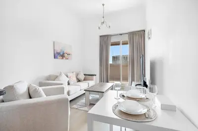 a white living room with a table and a couch at StoneTree - Furnished 1BR with Spacious Balcony in Dubai
