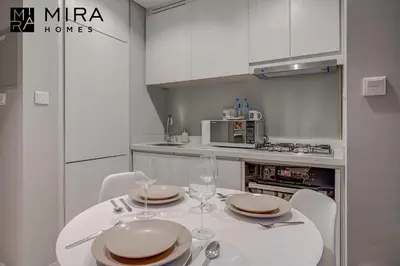 a white kitchen with a table with plates and wine glasses at Mira Holiday Homes - Serviced apartment in Zada Tower in Dubai