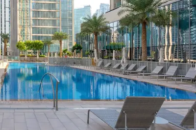 a large swimming pool with chairs and palm trees at Chic 2-Bedroom Downtown Gem in Dubai