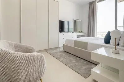 a white bedroom with a bed and a chair at Frank Porter - Bluebell Residence JVC in Dubai