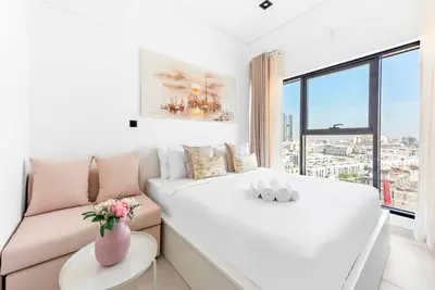 a white bed and a couch in a room with a window at Stylish Studio with Gym and Pool in Dubai